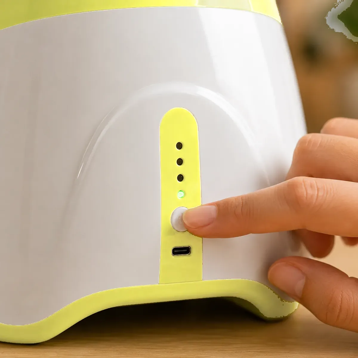 A finger presses the setting button on the back of the unit, above the four indicator lights